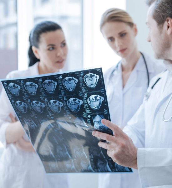 Revealing brain deformations. Qualified smart concentrated radiographs working at the laboratory and having discussion while holding computed tomography photo